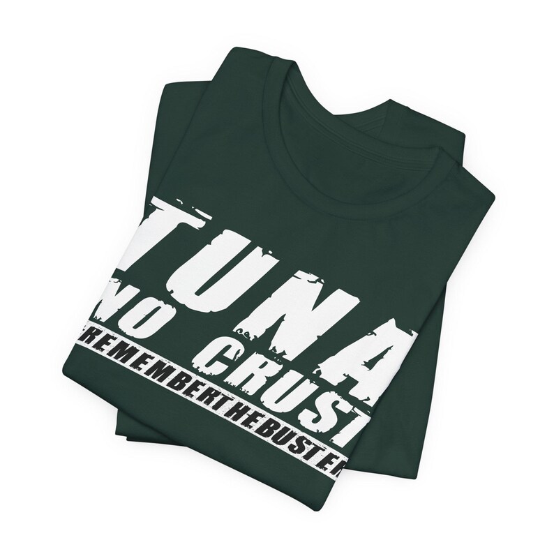Pu&ograve; includere: Una t-shirt verde scuro con testo bianco dall'aspetto consumato che recita TUNA NO CRUST REMEMBER THE BUSTER. La maglietta &egrave; piegata ordinatamente, mettendo in risalto la stampa grafica sulla parte anteriore del petto del capo.