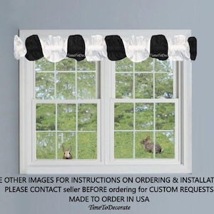 May include: Black and white ruffled valance with a polka dot pattern. The valance is made of a sheer fabric and is hung on a window with a view of green grass and a rabbit.