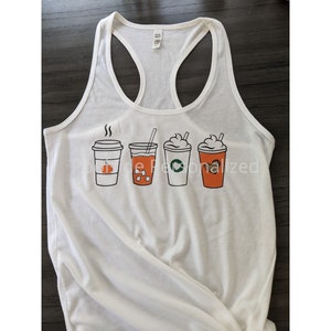 May include: White racerback tank top featuring a graphic of four different coffee drinks. The drinks include a pumpkin spice latte, iced coffee, a Starbucks-style drink, and a coffee with whipped cream. The tank top is a casual style.
