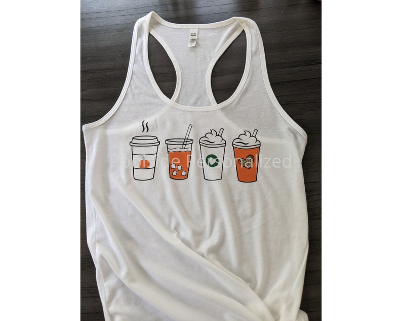 May include: White racerback tank top featuring a graphic of four different coffee drinks. The drinks include a pumpkin spice latte, iced coffee, a Starbucks-style drink, and a coffee with whipped cream. The tank top is a casual style.