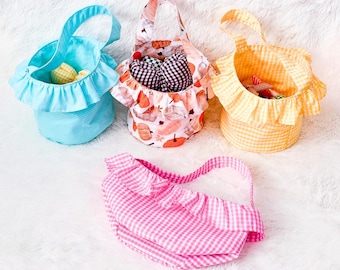 May include: Four fabric baskets in various colors and patterns. One is light blue with a polka dot pattern, another is orange and white gingham, a third is pink and white gingham, and the last is a floral pattern.