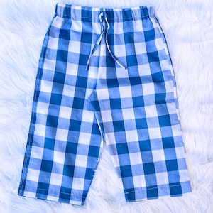 May include: Blue and white checkered shorts with a drawstring waist. The shorts are made of a lightweight fabric and are laid out on a white, fluffy surface. Three spools of thread in blue and green are in the upper left corner.