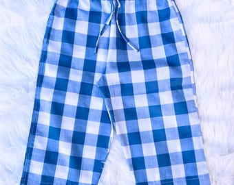 May include: Blue and white checkered shorts with a drawstring waist. The shorts are made of a lightweight fabric and are laid out on a white, fluffy surface. Three spools of thread in blue and green are in the upper left corner.