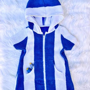 May include: A blue and white striped hooded towel robe with a front zipper and a pocket. The robe has short sleeves and is made of a soft, absorbent material. Two spools of thread are in the pocket.