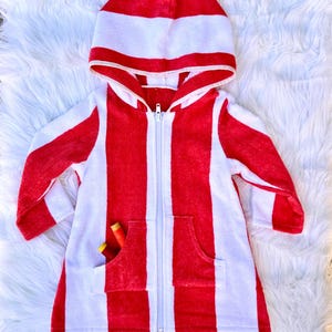 May include: A red and white striped hooded towel robe with a full-length zipper and two front pockets. The robe has a hood and long sleeves. The robe is made of a soft, absorbent material. Two spools of thread are in the pocket.