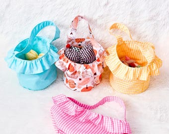 May include: Four fabric baskets in various colors and patterns. One is light blue with a polka dot pattern, another is orange and white gingham, a third is pink and white gingham, and the last is a floral pattern.