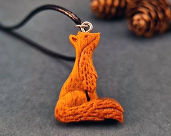 May include: A wooden fox pendant necklace with a brown leather cord. The fox is carved in detail and has a reddish-brown color.