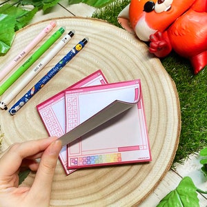 Op de afbeelding: Twee roze en witte notitiebloksets met een vensterontwerp. De notitieblokken hebben een rasterpatroon en de tekst "Lemoncholy Art" in de rechterbenedenhoek.