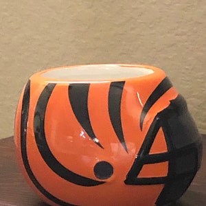 May include: Orange and black ceramic planter shaped like a football helmet.