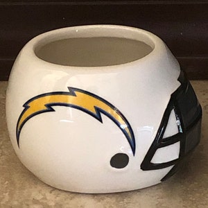 May include: White ceramic planter shaped like a football helmet with a blue and yellow lightning bolt design. The helmet has a black facemask.