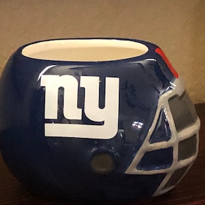 May include: A blue and white ceramic planter shaped like a football helmet with the New York Giants logo, "NY", on the front.