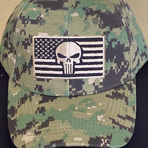 May include: A green camouflage baseball cap with a white and black American flag patch featuring a black skull and crossbones.