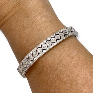 May include: A silver bangle bracelet with a geometric design of small diamonds set in a repeating pattern.