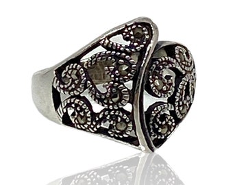 May include: A silver ring with a delicate, intricate design featuring a swirl pattern. The ring is set with small, dark gray gemstones.