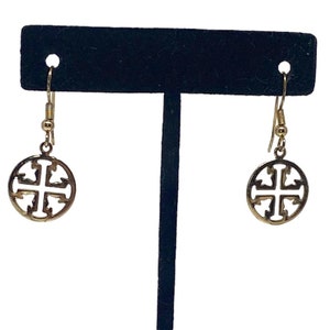 May include: Gold tone dangle earrings with a circular design featuring a cross cutout. The earrings are on a black display stand.