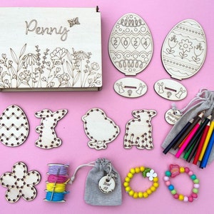 Personalised Wooden Easter Box -19.5cm x 14.5cm x 3cm.5 wooden embroidery shapes, 4 colours of cotton thread, 1 metal needle, 2 wooden easter egg shapes on a base, 12 colouring pencils, wooden bead kit to make 2 bracelets.