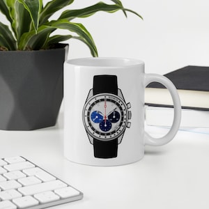 Könnte beinhalten: Weiße Keramiktasse mit einem schwarzen und silbernen Chronographen-Uhrendesign. Das Zifferblatt der Uhr hat blaue und rote Akzente und den Text "TACHYMETER" auf der Lünette.