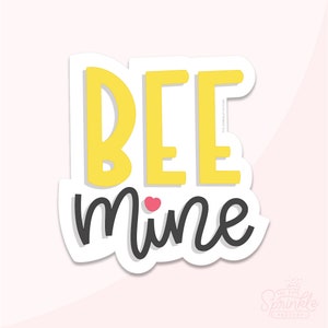 May include: A white sticker with a yellow and black design. The text "BEE mine" is written in black with a small pink heart between the words.