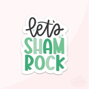 Op de afbeelding: Groene en zwarte sticker met de tekst "Let's Shamrock" in een leuk, handgeschreven lettertype.