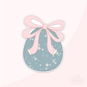 May include: An egg-shaped cookie cutter with a light blue speckled design and a pink bow. The bow has long ribbons with scalloped edges. The cookie cutter is on a white background.