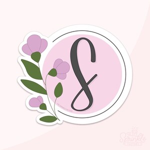 May include: A pink and white circle sticker with a black cursive letter "S" and a floral design with pink flowers and green leaves. The text "The Sprinkle Factory" is at the bottom of the sticker.