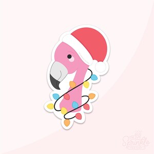 Puede incluir: Adhesivo de un flamenco rosa con un gorro de Papá Noel rojo y envuelto en una cadena de luces navideñas de colores. El flamenco tiene un pico negro y está sobre un fondo rosa claro. El adhesivo es de The Sprinkle Factory.