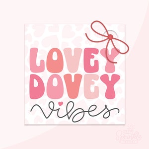 May include: A pink and white gift tag with a red string bow. The tag has a pink and white leopard print background with the text "Lovey Dovey Vibes" in pink and white letters.