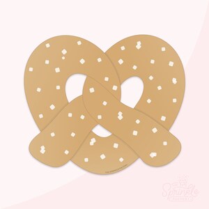 Puede incluir: Un pretzel marrón con chispas blancas, con forma de pretzel. El pretzel está sobre un fondo rosa con el texto "The Sprinkle Factory" en pequeñas letras blancas en la parte inferior.