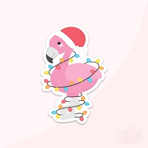 Puede incluir: Una pegatina de un flamenco rosa con un gorro de Papá Noel y envuelto en luces navideñas de colores. El flamenco tiene un pico negro y está de pie sobre patas blancas. La pegatina tiene un borde blanco y un fondo rosa claro.