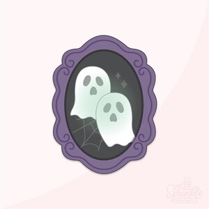 Puede incluir: Un cortador de galletas ovalado de color morado con un marco festoneado decorativo. El diseño interior muestra dos fantasmas de color verde pálido con ojos y bocas oscuros, sobre una telaraña negra y dos pequeñas estrellas.