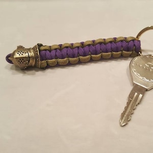 May include: A purple and green paracord keychain with a metal helmet charm and a silver key attached to a silver key ring.