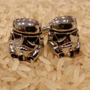 May include: A pair of silver cufflinks featuring a detailed design of a Stormtrooper helmet from Star Wars.
