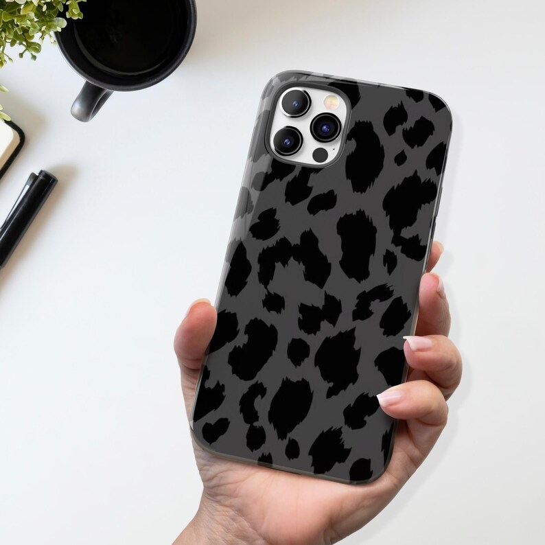 May include: A smartphone case with a gray and black leopard print design. The case is held in a hand, showcasing the glossy finish and the camera module. The case is designed to fit a smartphone.