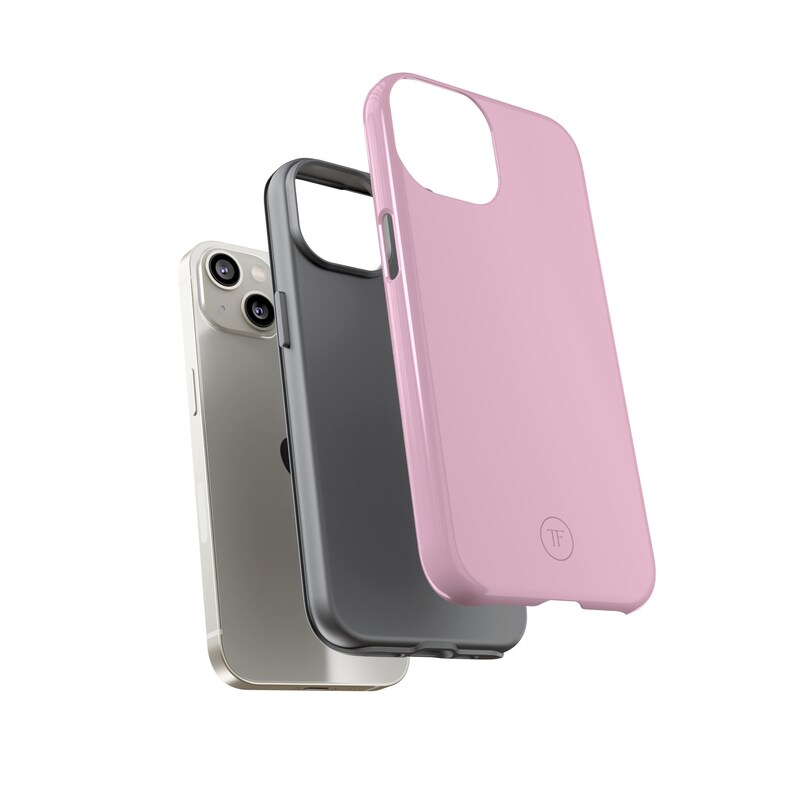 May include: Three phone cases stacked on top of each other. The bottom case is a silver iPhone case. The middle case is a black phone case. The top case is a pink phone case with a small circle logo that says "TF".