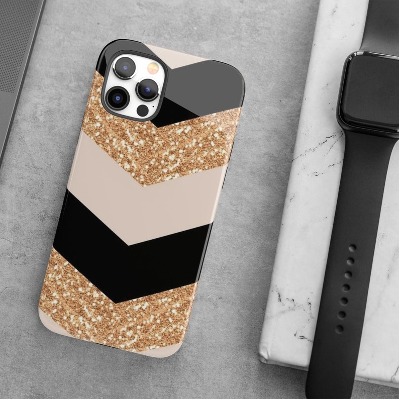 Puede incluir: Una funda de tel&eacute;fono negra y beige con un patr&oacute;n de chevron de purpurina dorada. La funda tiene una parte posterior transparente y un borde negro. La funda de tel&eacute;fono est&aacute; dise&ntilde;ada para un iPhone.