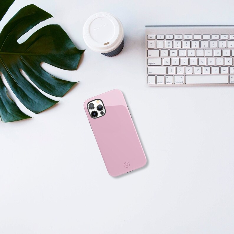 May include: A pink phone case with a clear camera lens cover. The case has a small, circular logo on the back.