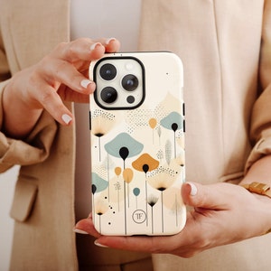 K&ouml;nnte beinhalten: Eine wei&szlig;e iPhone-H&uuml;lle mit einem Blumendesign mit blauen, gelben und beigefarbenen Blumen. Die H&uuml;lle hat eine schwarze Kamera-Erhebung und die Buchstaben "TF" in einem Kreis auf der R&uuml;ckseite.