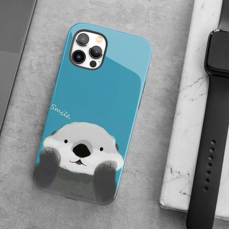 May include: A blue phone case with a cartoon sea otter with the word "Smile." printed on the case.