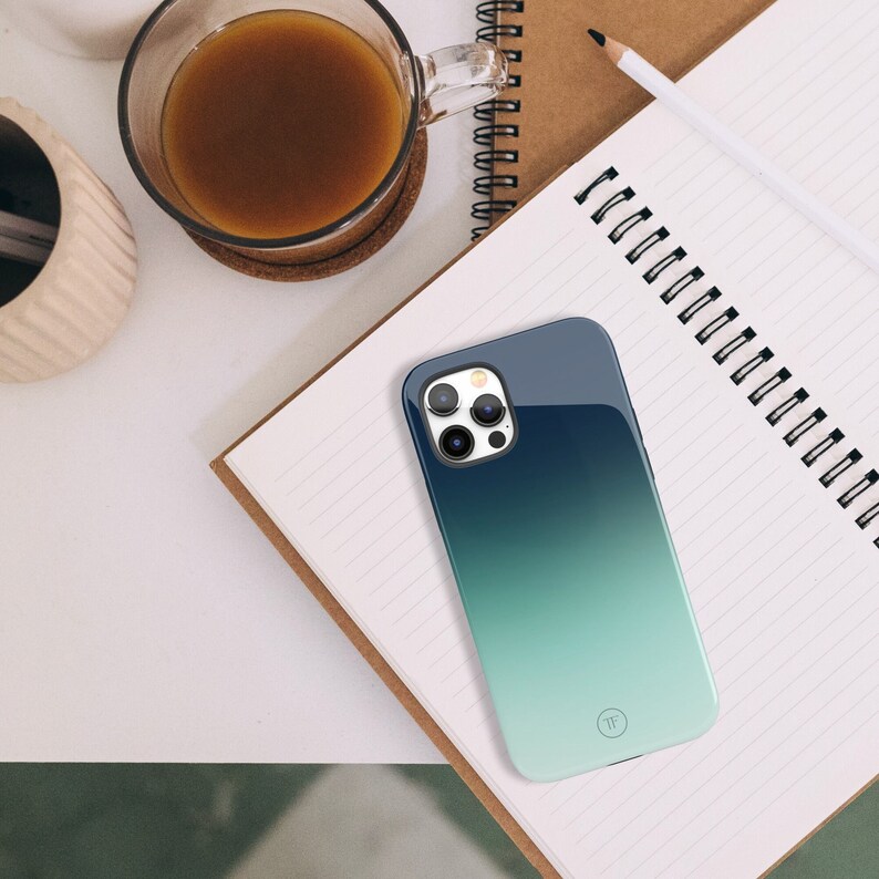 May include: A blue and green gradient phone case with a clear camera lens cover. The case has a small, white circle with the letter "T" inside.