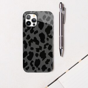 May include: A smartphone case with a gray leopard print design. The case is glossy and has a black camera lens area. A silver pen rests next to the phone case on a white surface.