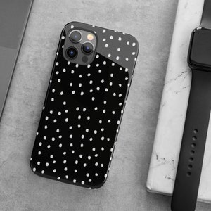 May include: A black phone case with a white polka dot pattern. The case has a clear back and a black frame. The camera lenses are visible on the back of the case.