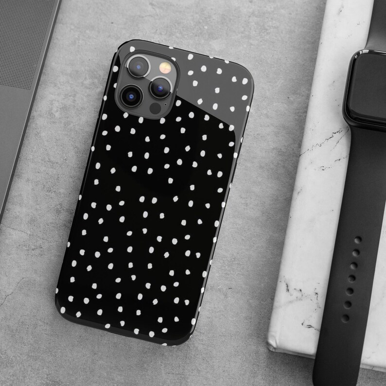 May include: A black phone case with a white polka dot pattern. The case has a clear back and a black frame. The camera lenses are visible on the back of the case.