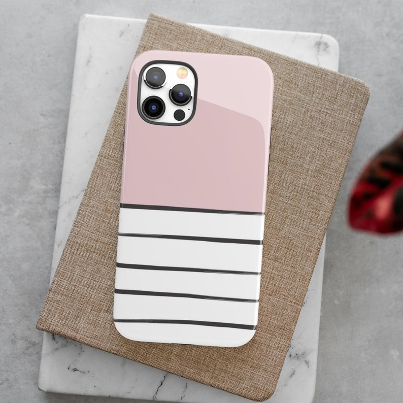 May include: A pink and white striped phone case with a black camera lens. The case is made of a hard plastic material and has a glossy finish.