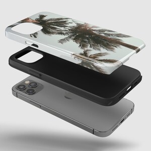 May include: A clear phone case with a tropical palm tree design. The case is shown layered over a black phone case and a gray iPhone.