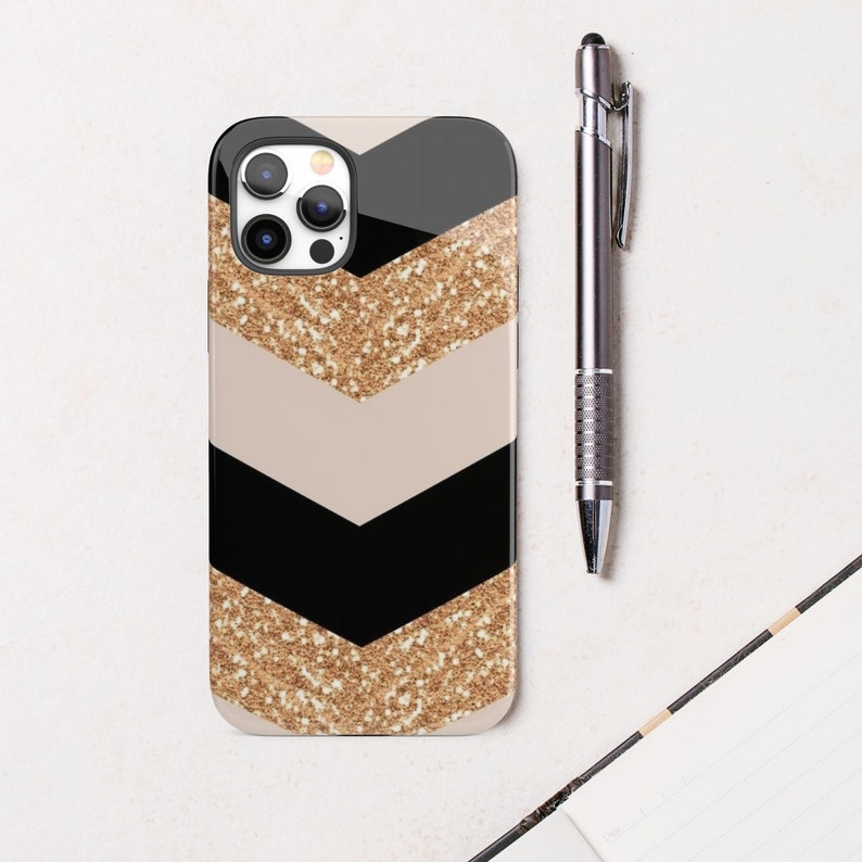 Puede incluir: Una funda de tel&eacute;fono negra y beige con un patr&oacute;n de chevron de purpurina dorada. La funda tiene un recorte para la c&aacute;mara del tel&eacute;fono.