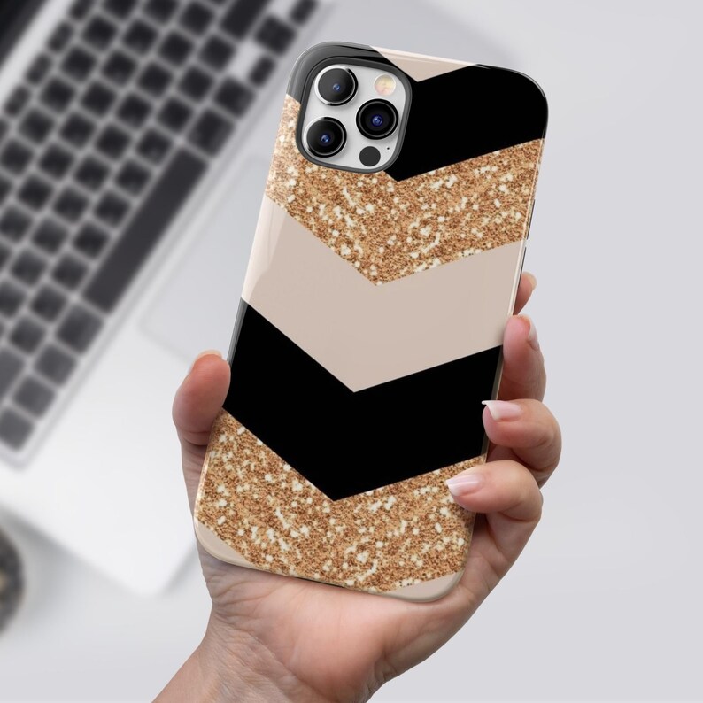 Puede incluir: Una funda para tel&eacute;fono de color negro y dorado con purpurina y un patr&oacute;n de chevron. La funda tiene un recorte para la lente de la c&aacute;mara.