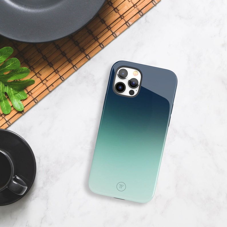 May include: A blue and green gradient phone case with a clear camera lens cover and a small circle logo with the letters "TF" in the center.