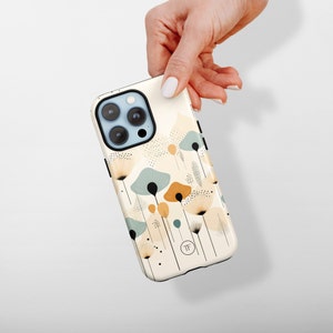 K&ouml;nnte beinhalten: Eine wei&szlig;e iPhone-H&uuml;lle mit einem Blumendesign mit abstrakten Blumen in Blaut&ouml;nen, Gelb und Braun. Die H&uuml;lle hat einen schwarzen Kameraausschnitt und einen kleinen schwarzen Kreis mit den Buchstaben "TF" in der Mitte.