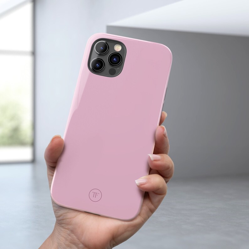 May include: A pink phone case with a clear camera lens cover and a small circle logo with the letters "TF" in the center.