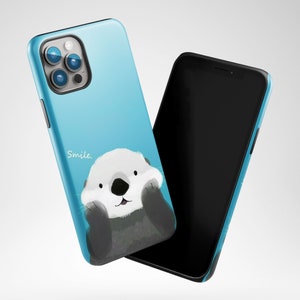 May include: A blue phone case with a cartoon sea otter and the word "Smile." The case is designed for a phone with a triple lens camera.